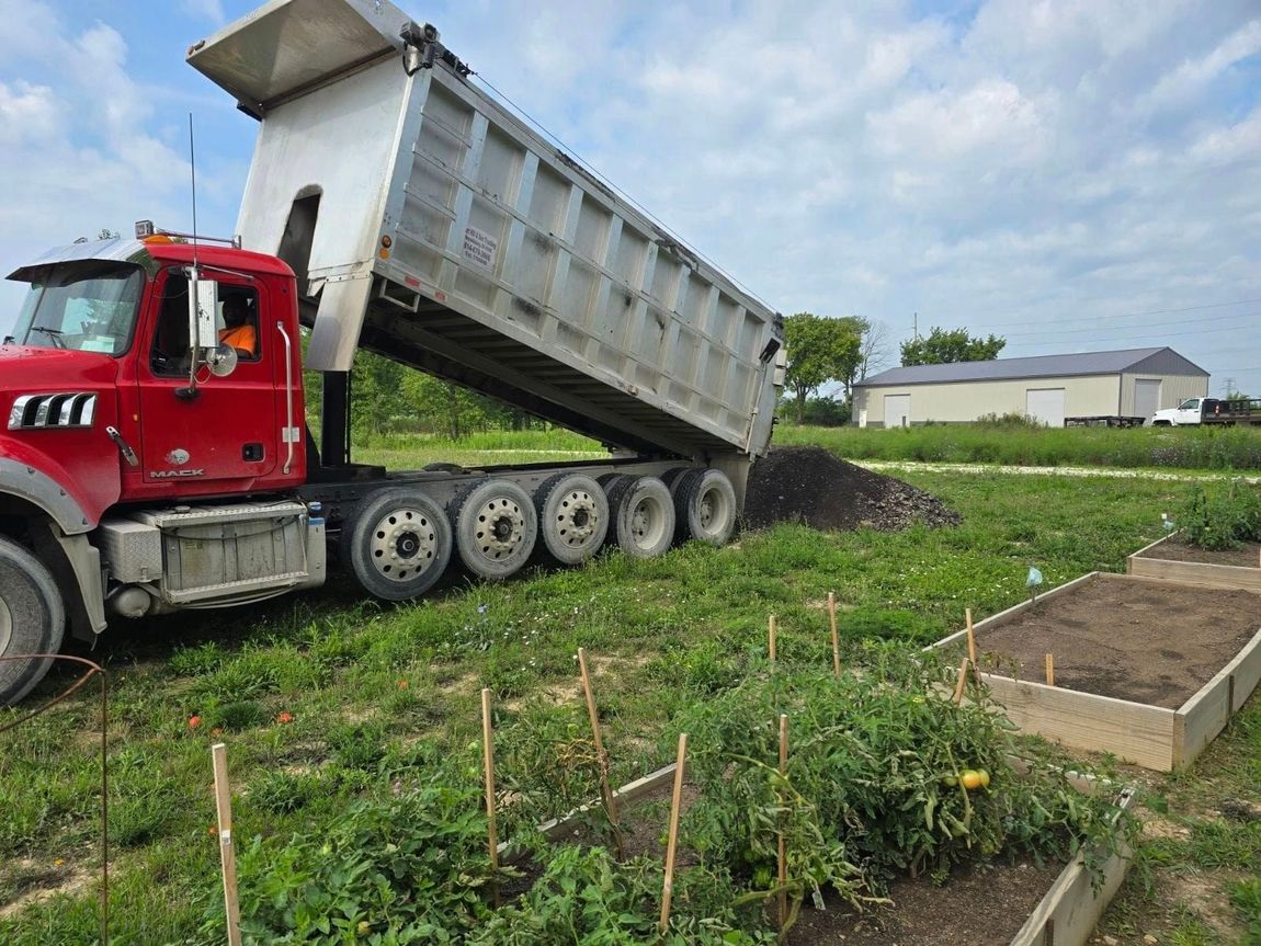 A dump truck is loading dirt into a garden.