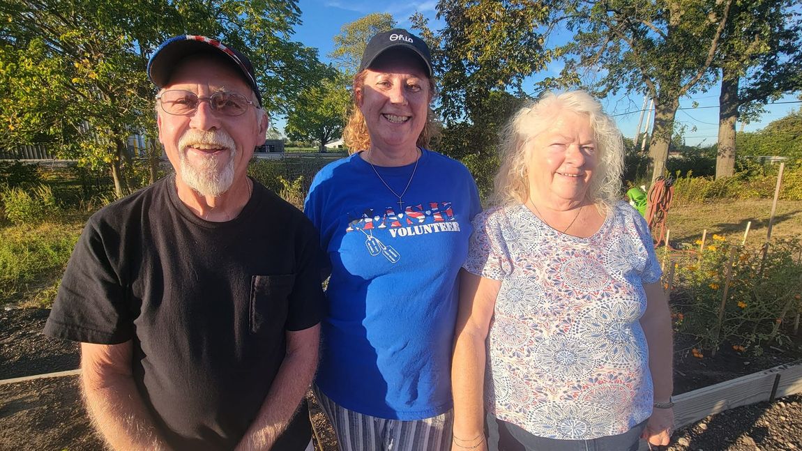 A man and two women are standing next to each other in a park.