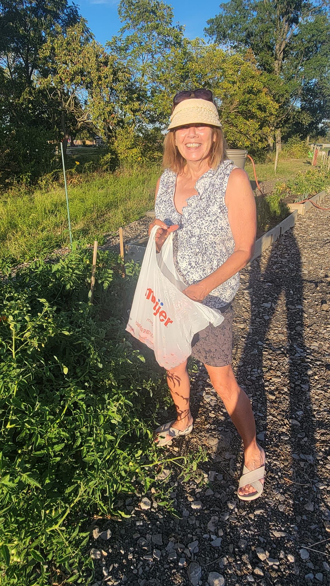 A woman is standing in a garden holding a white bag.