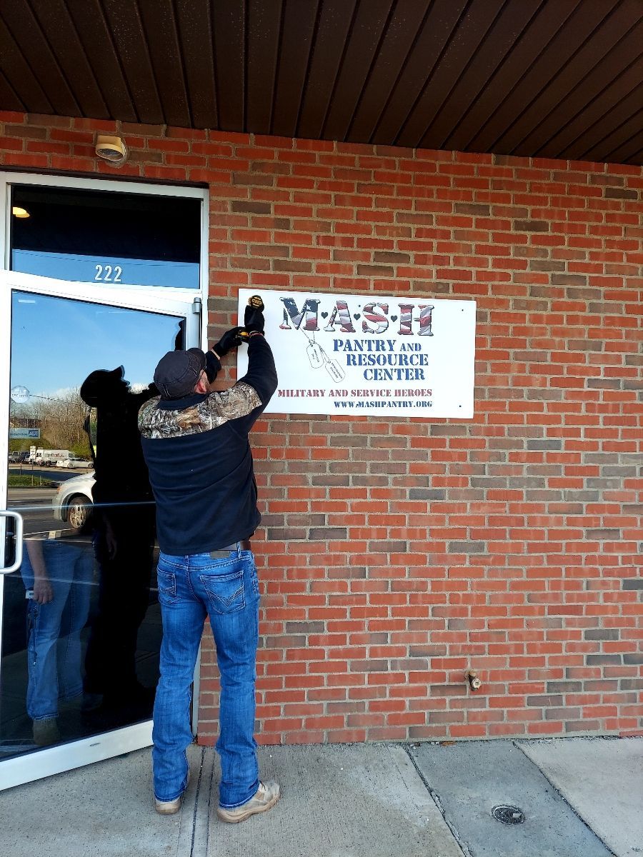 A man is putting a sign on a brick building that says mashpantry