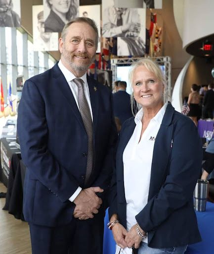 A man in a suit and tie stands next to a woman in a white shirt