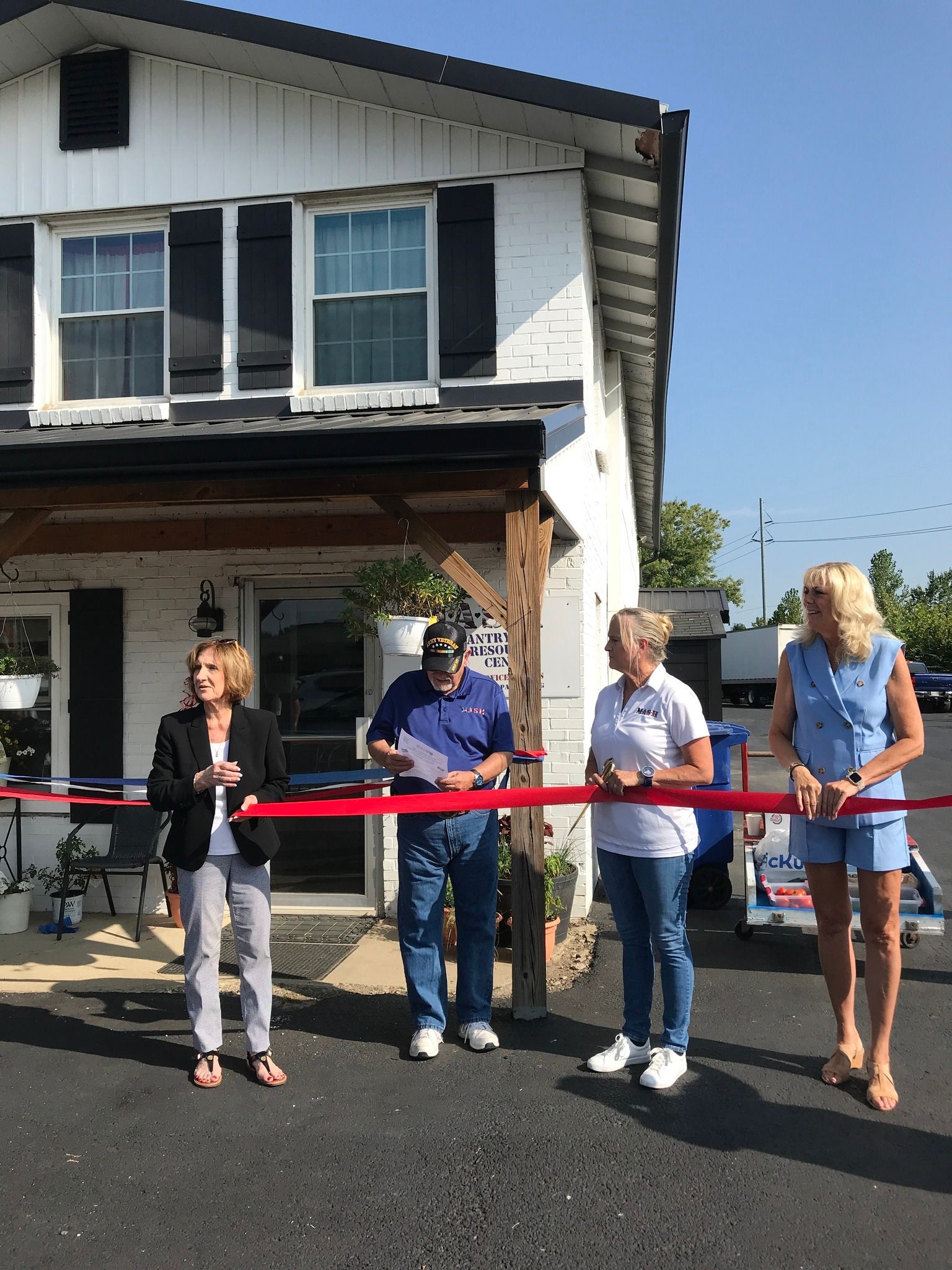 A group of people are cutting a red ribbon in front of a house