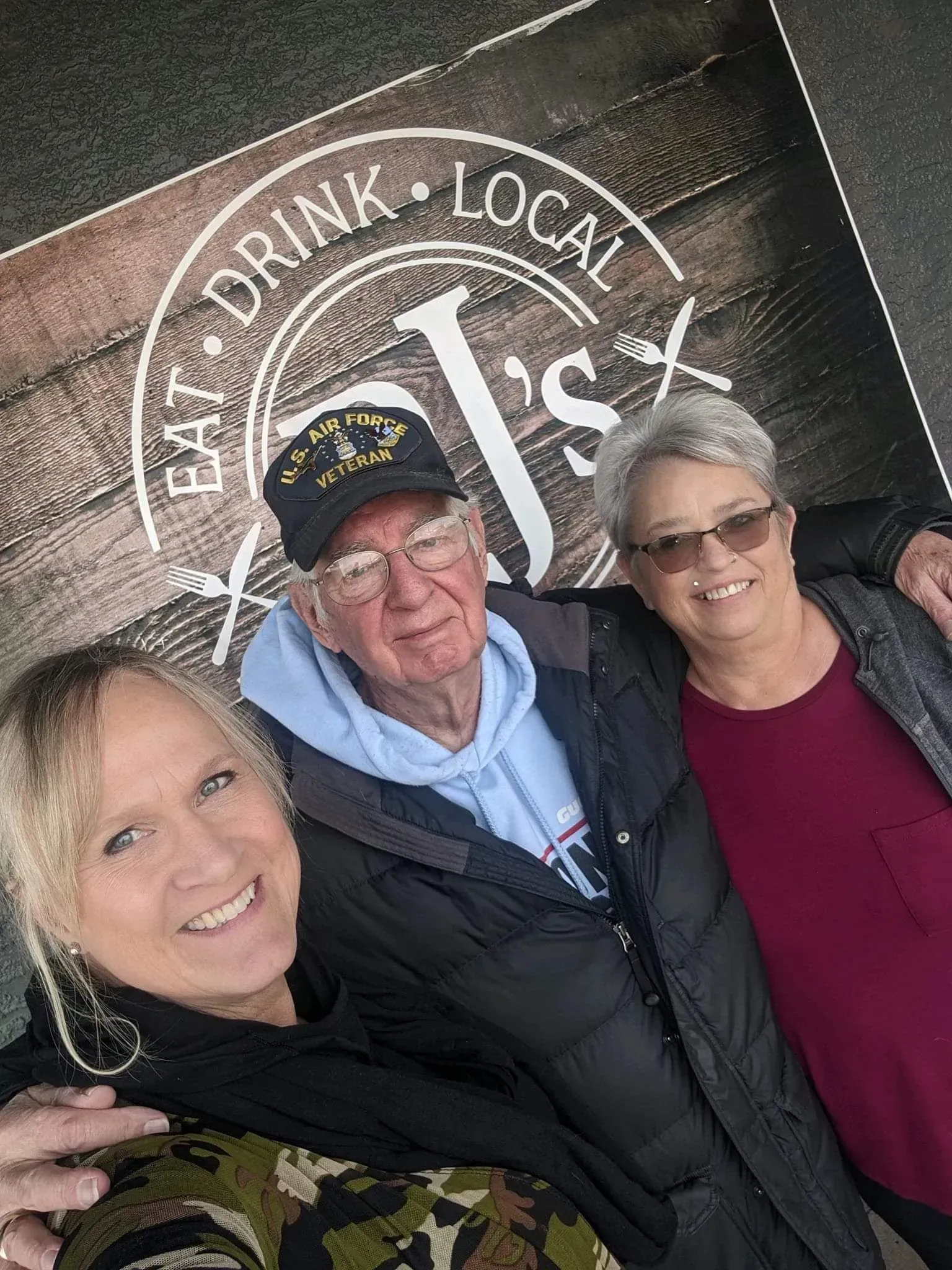 Three people are posing for a picture in front of a sign that says `` eat drink local ''.