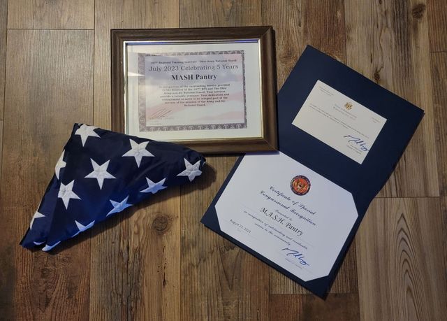 A framed certificate , an american flag , and a folder are on a wooden floor.