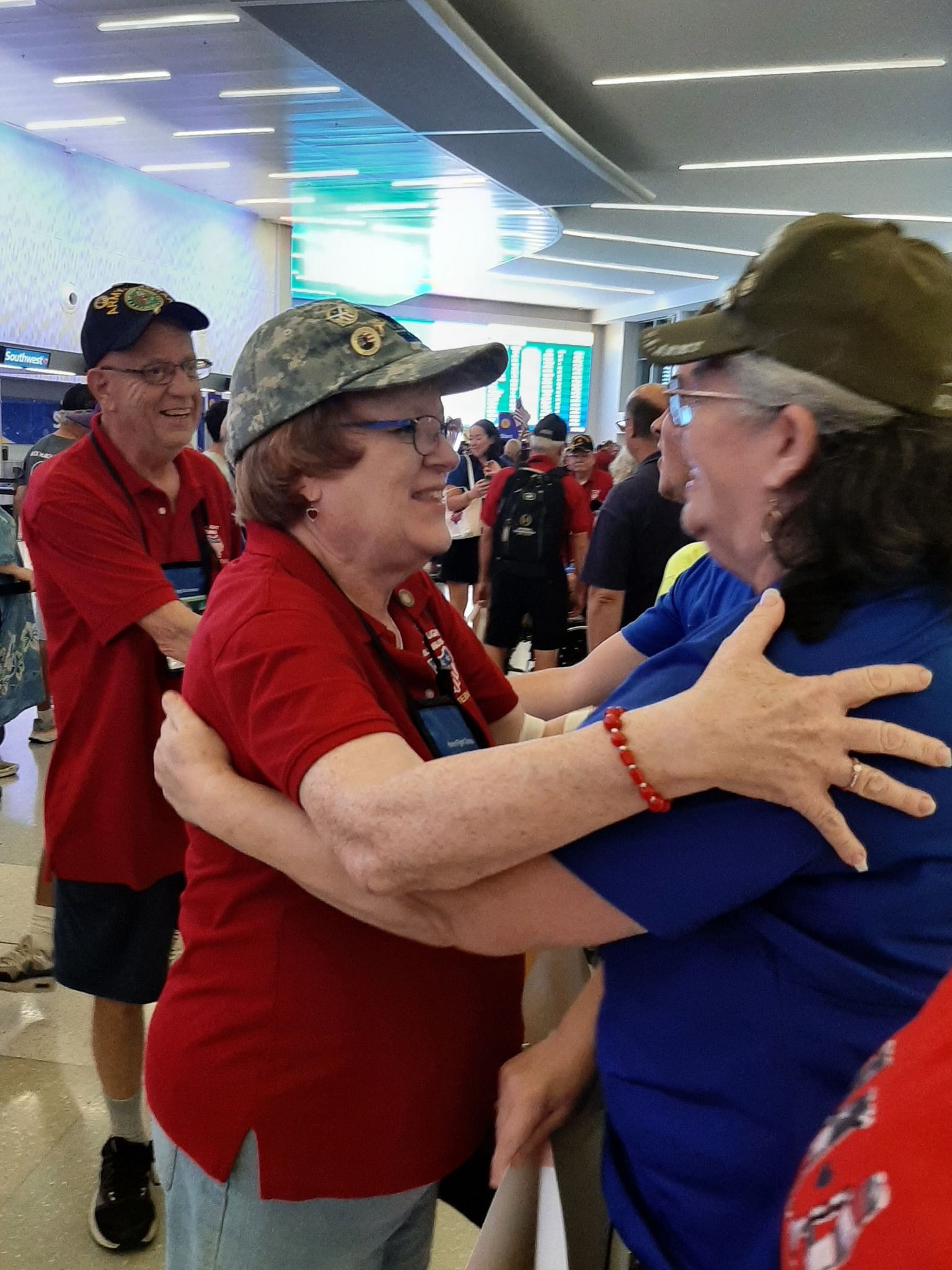 A woman in a red shirt is hugging another woman in a blue shirt.