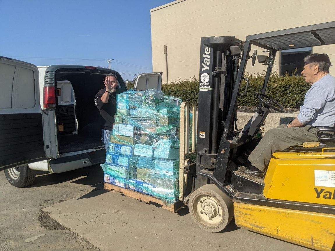 A man is sitting in a forklift loading a pallet of diapers into a van.