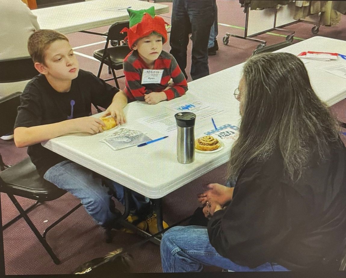 A boy wearing an elf hat sits at a table with a woman