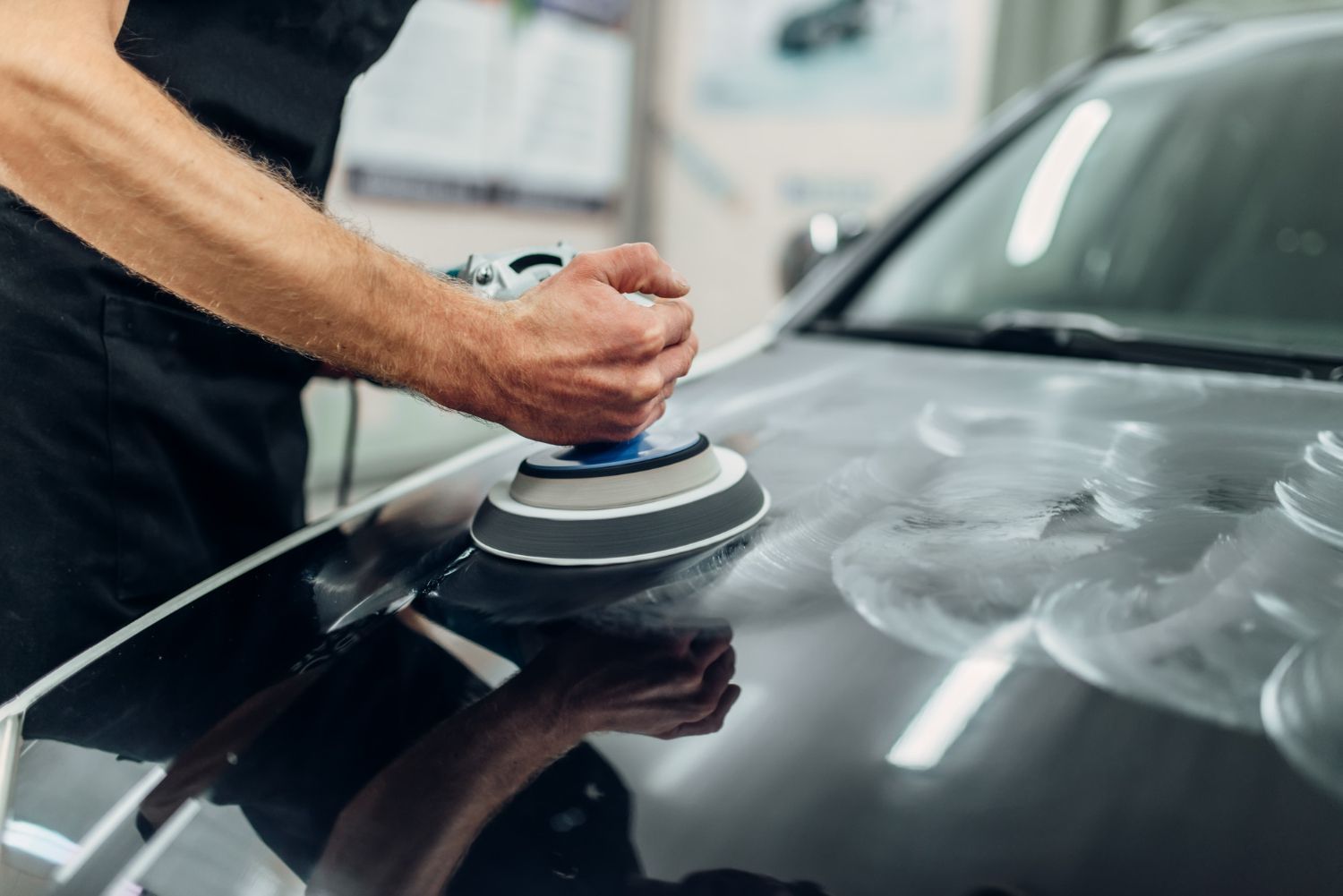 A man is polishing a black car with a machine.
