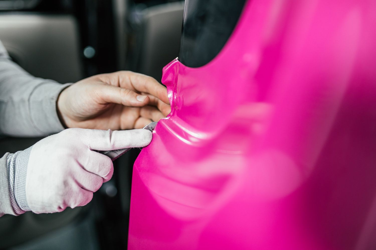 A person is wrapping a pink car with pink vinyl.