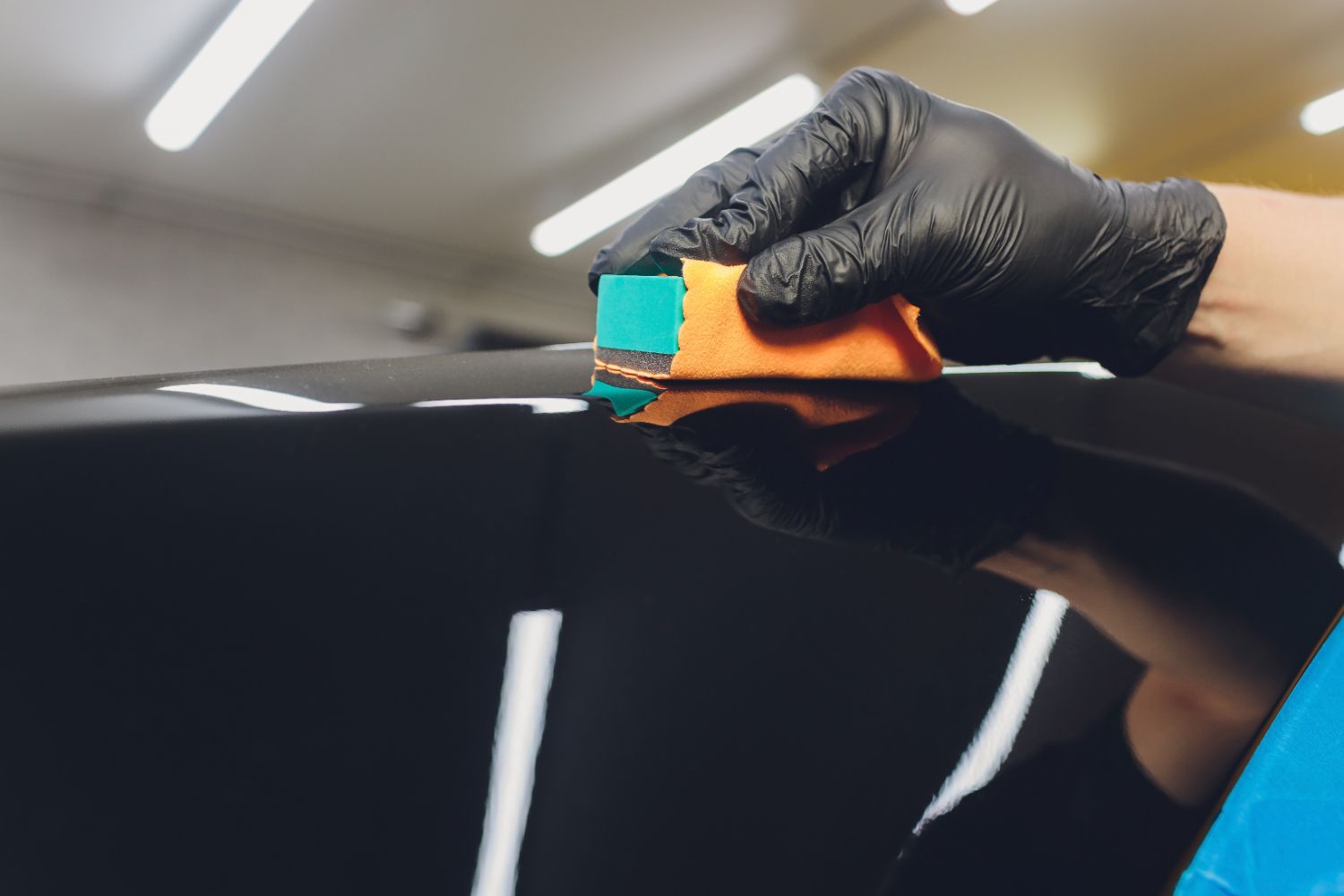 A person wearing black gloves is cleaning a car with a sponge.
