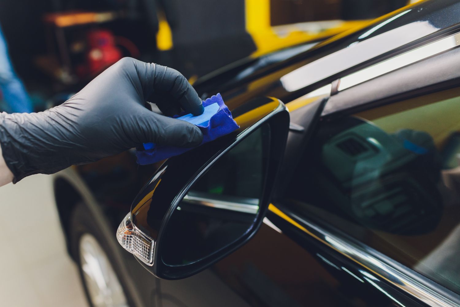 A person is applying ceramic coating to the side mirror of a car.