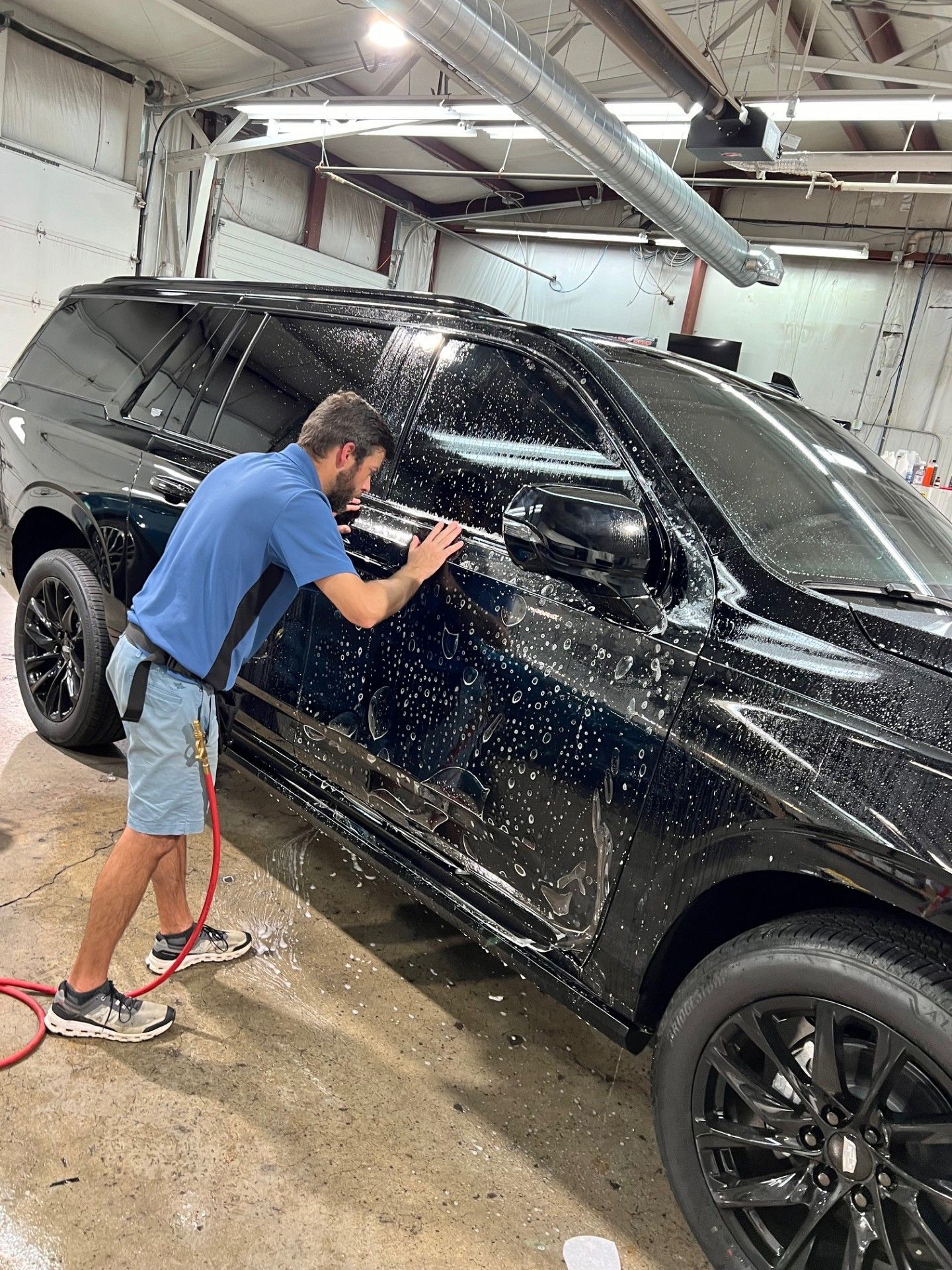 A man is washing a black suv in a garage.