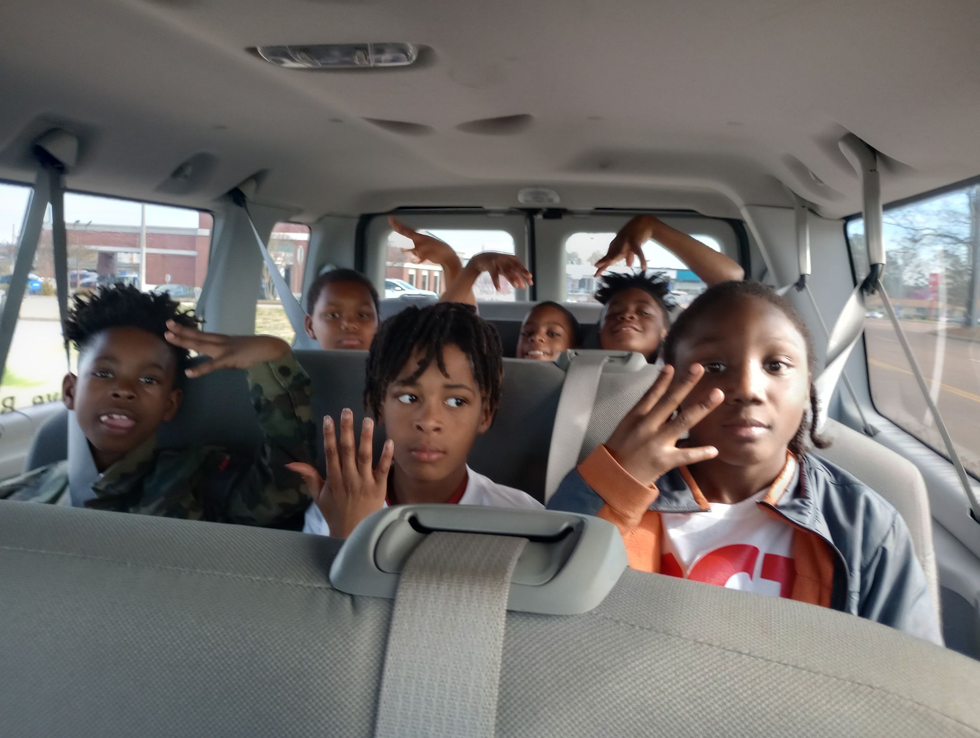Group of children in a van, making hand gestures.  They are smiling and looking at the camera.
