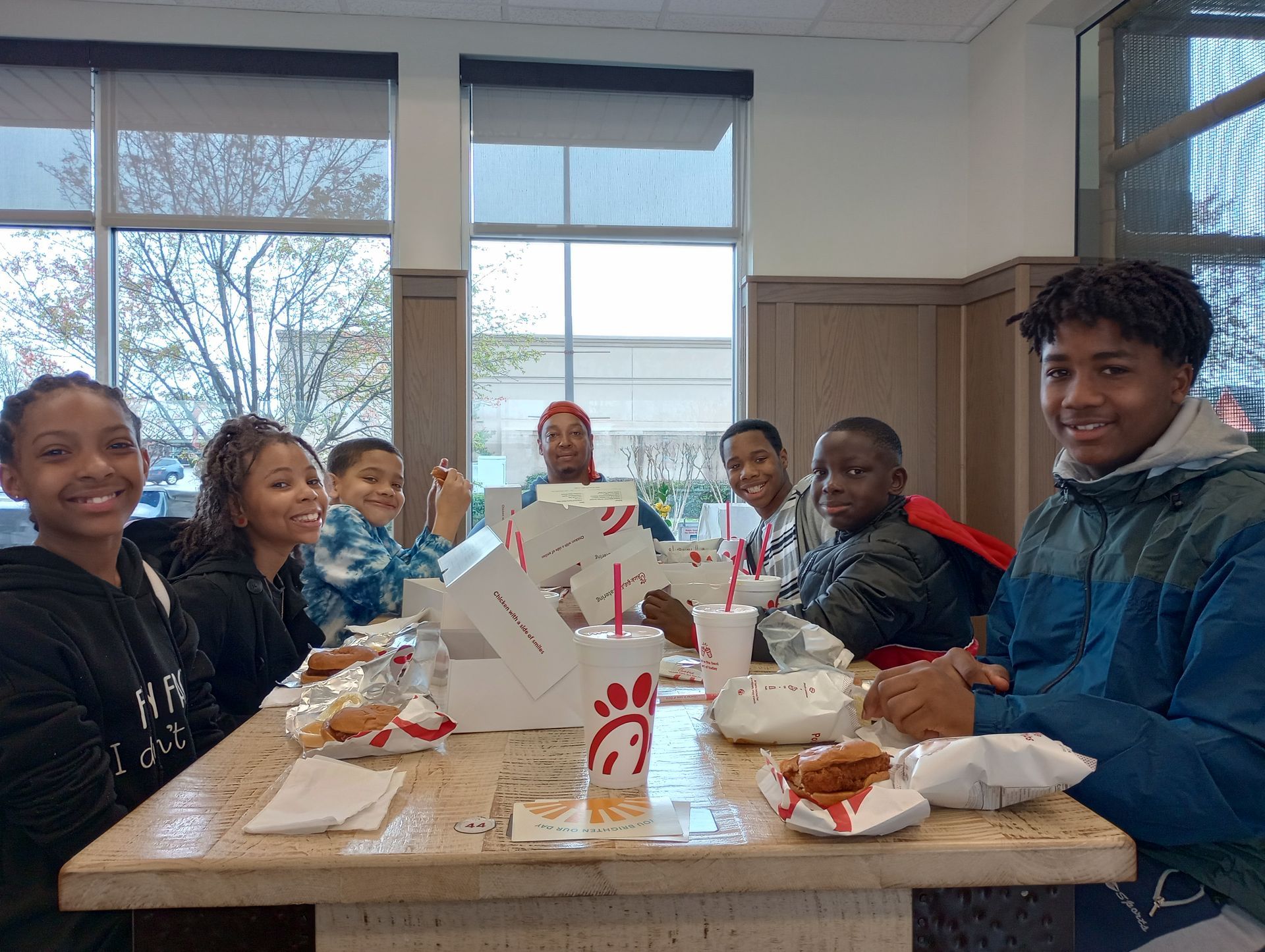 Group of diverse young people smiling while eating at a Chick-fil-A table. They appear to be enjoying a meal with food and drinks.