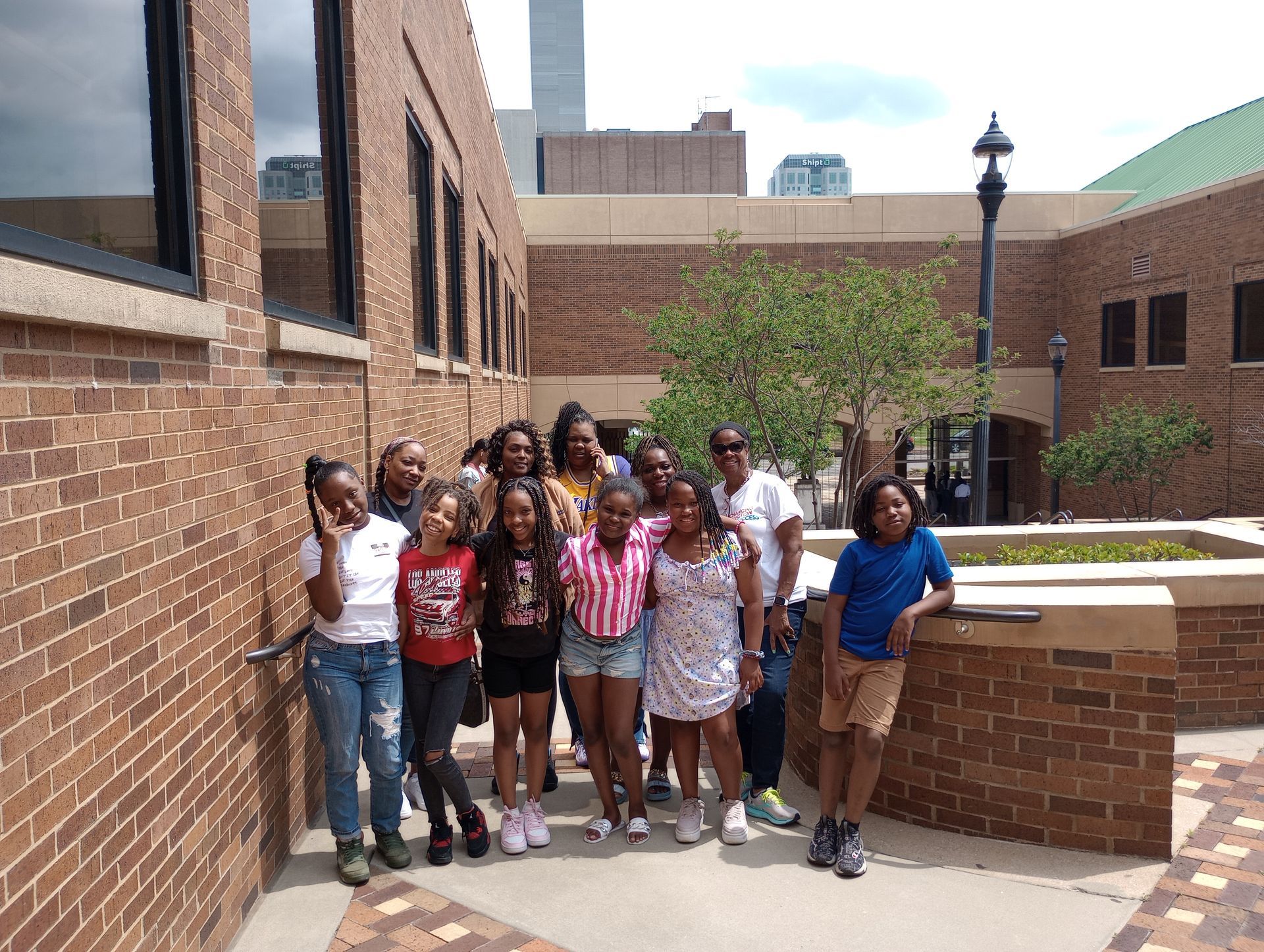 A group of people poses outdoors, with many children and some adults, in front of a brick building with dark windows.