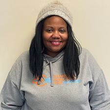 Woman with black hair wearing a gray beanie and hoodie smiles at the camera.