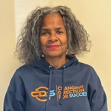 A woman with gray curly hair, wearing a blue hoodie with 