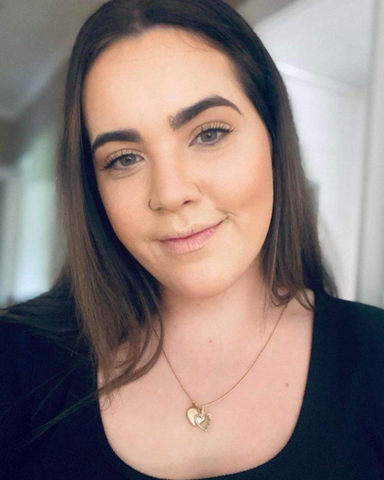 Woman with brown hair, wearing a black shirt and heart pendant, smiling. — Wow! Excellence in Hair in Toowoomba, QLD