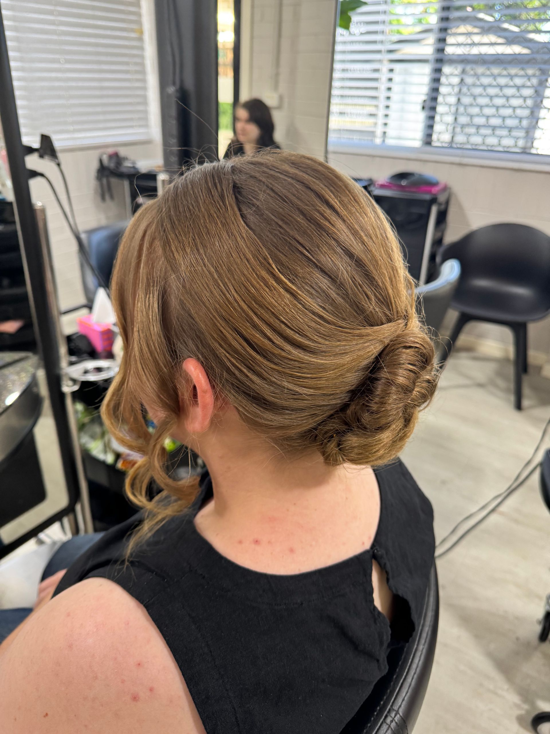 Woman with blonde updo hairstyle in a salon, back view.