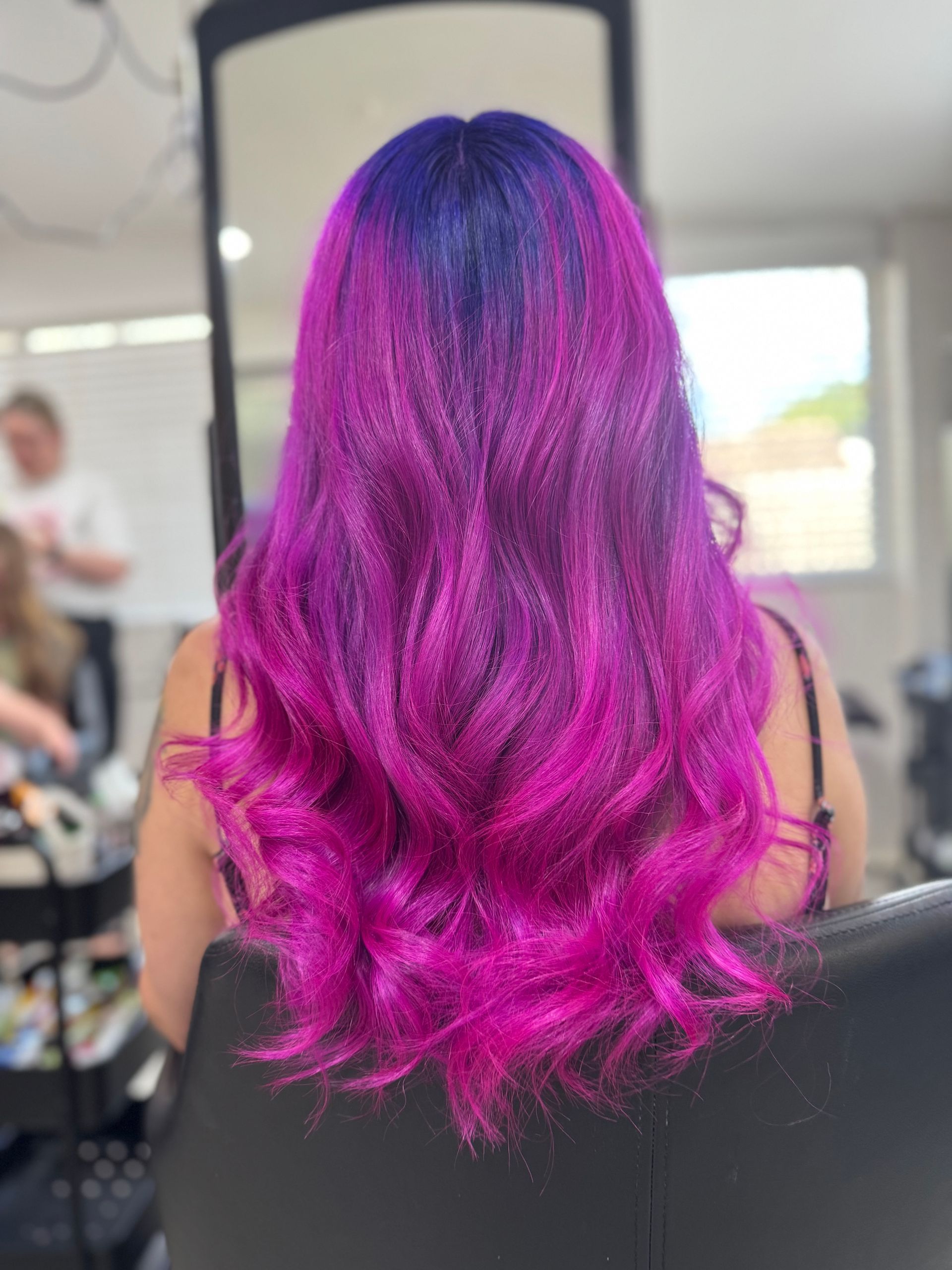 Woman with long, wavy hair colored vibrant purple and blue in a salon setting.