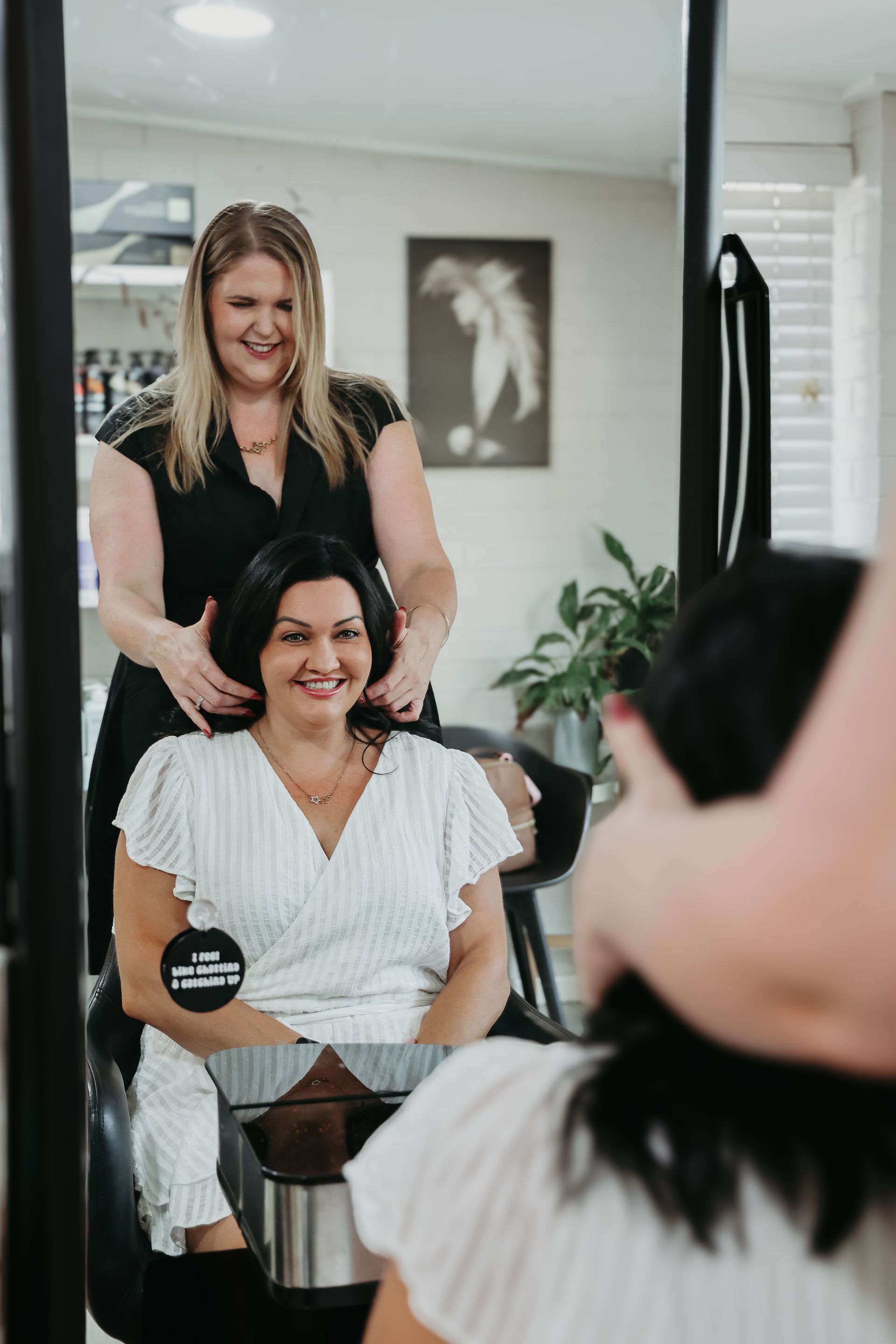 Woman getting her hair styled by another woman in a salon, smiling.