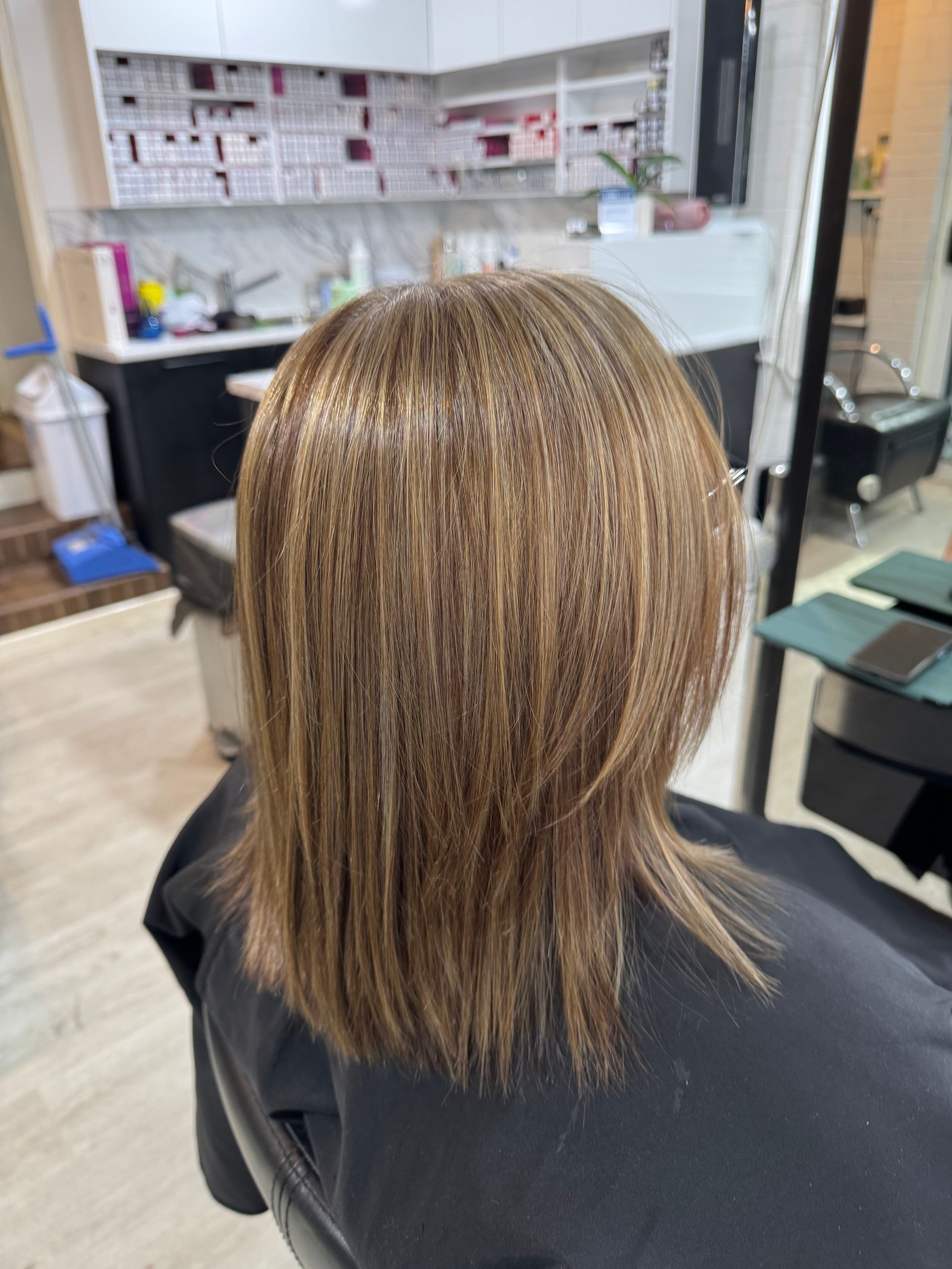 Woman with layered brown hair, highlighted with lighter tones, in a salon chair.