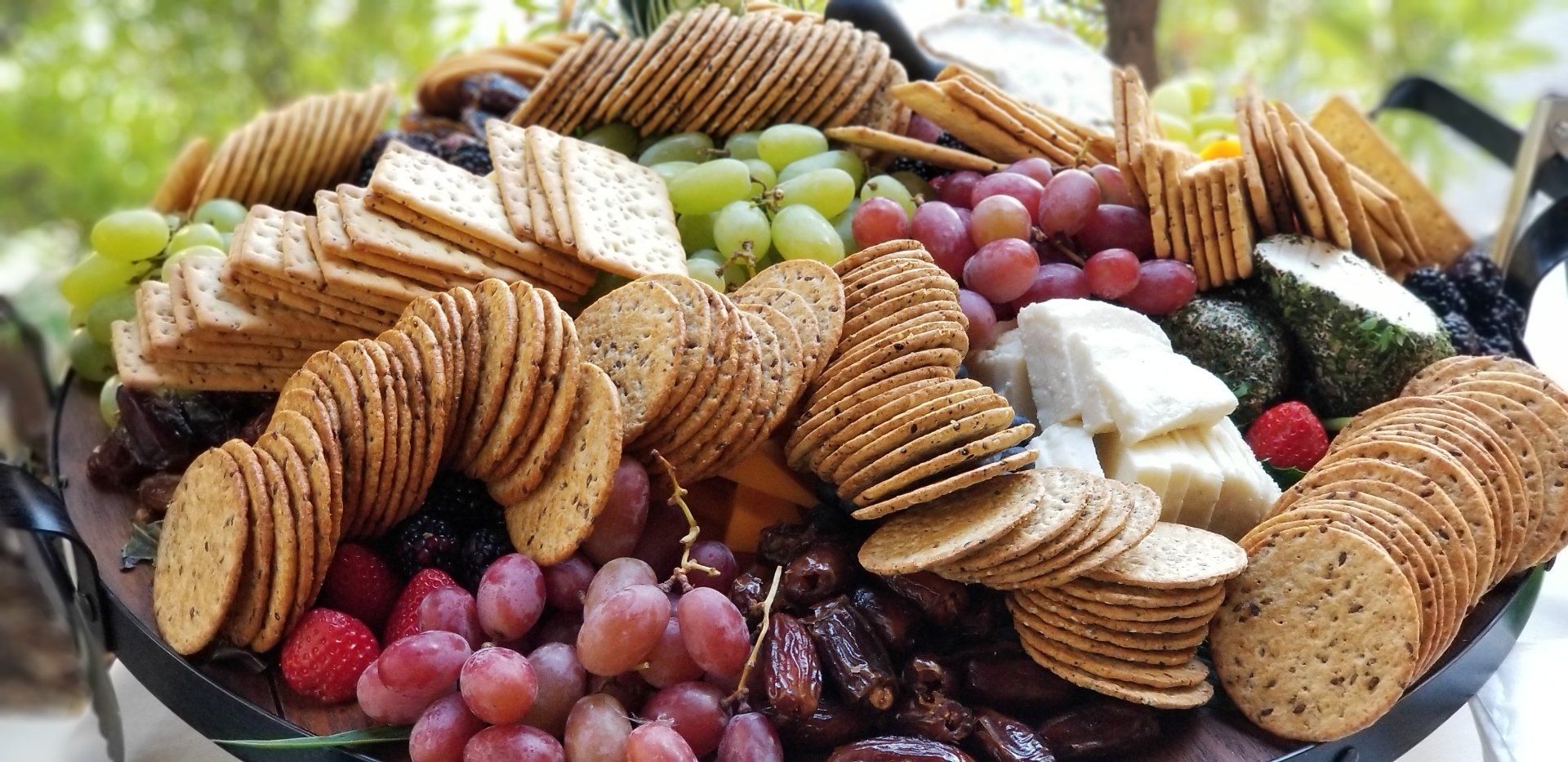 A tray filled with crackers , grapes , cheese and fruit.