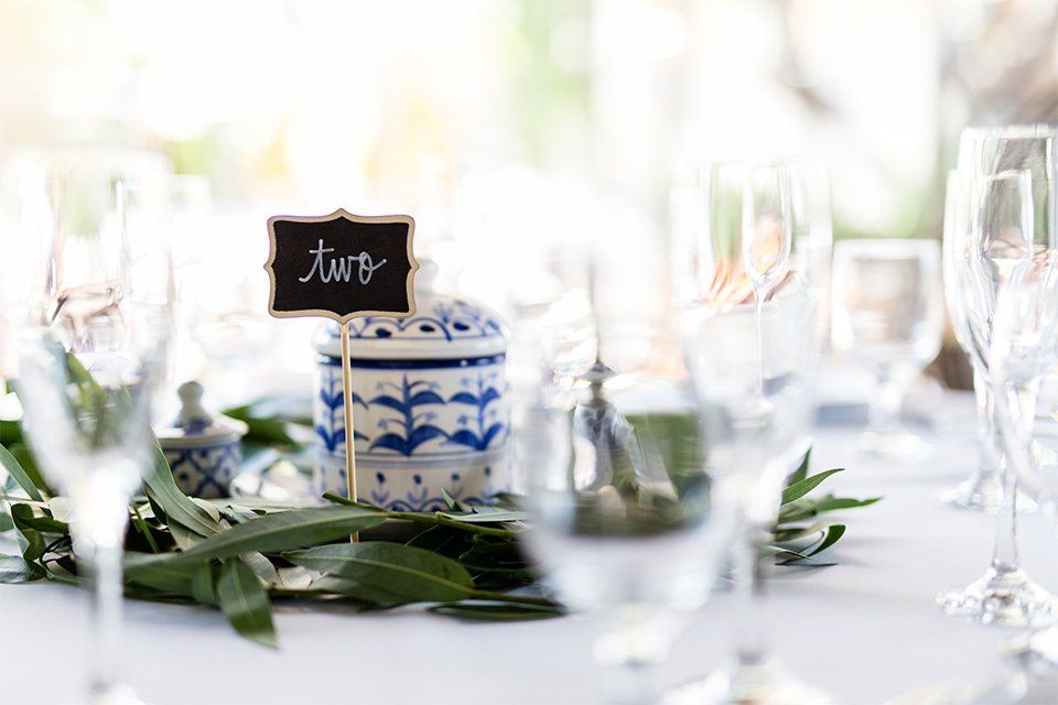 A table set for a wedding reception with wine glasses and a small sign that says two.