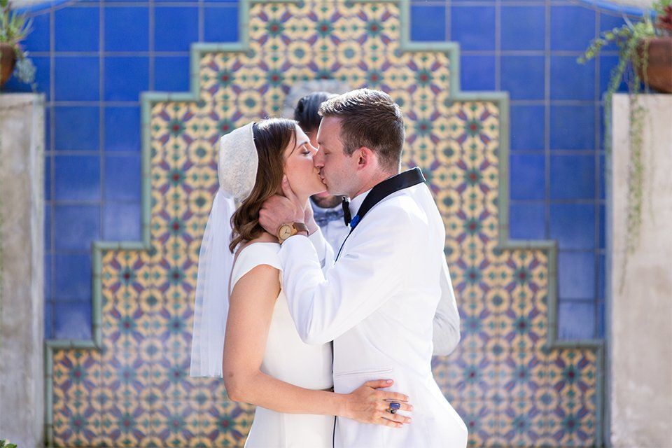 A bride and groom kissing in front of a blue tiled wall.