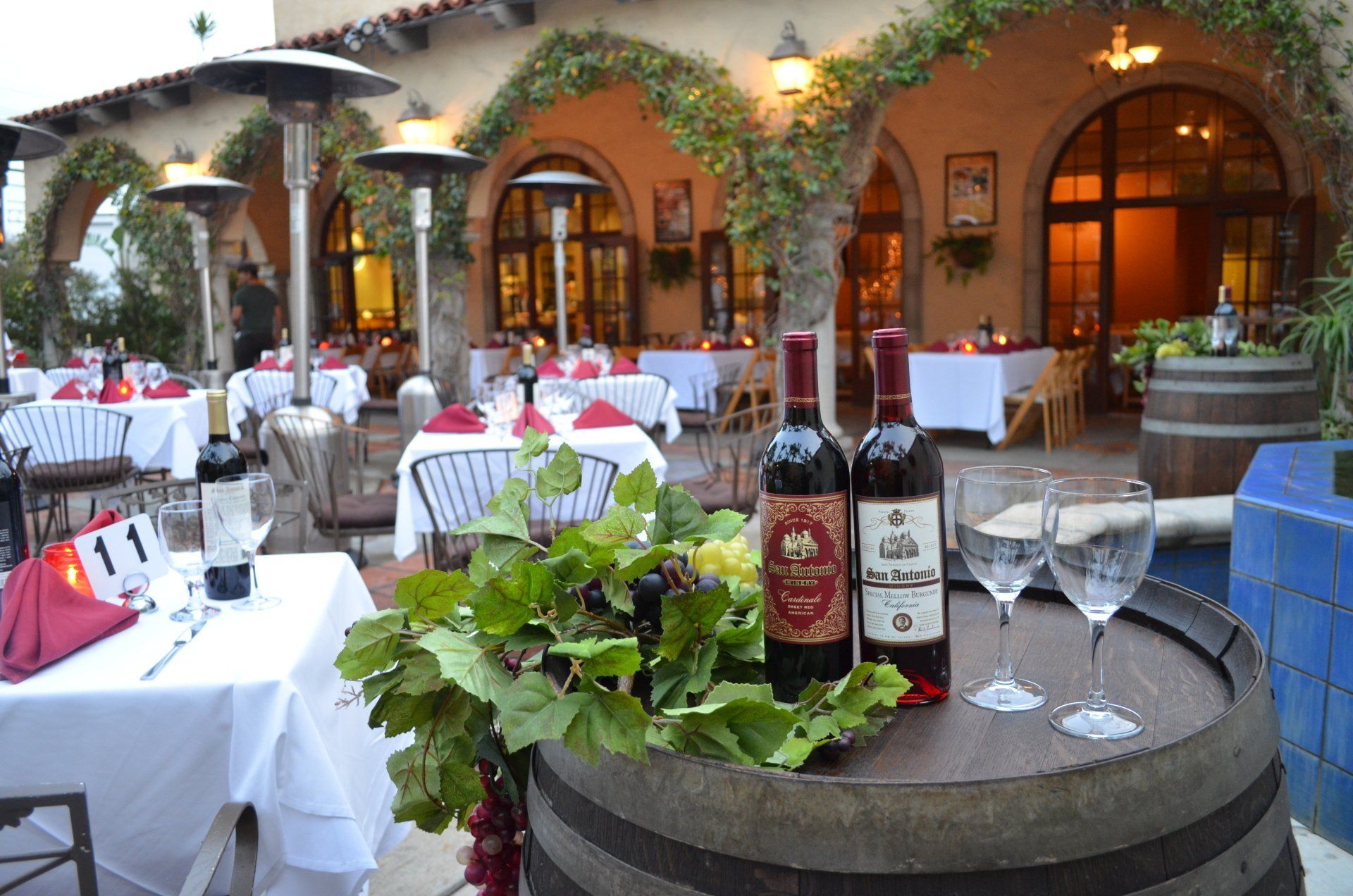 Two bottles of wine sit on a barrel in front of a restaurant