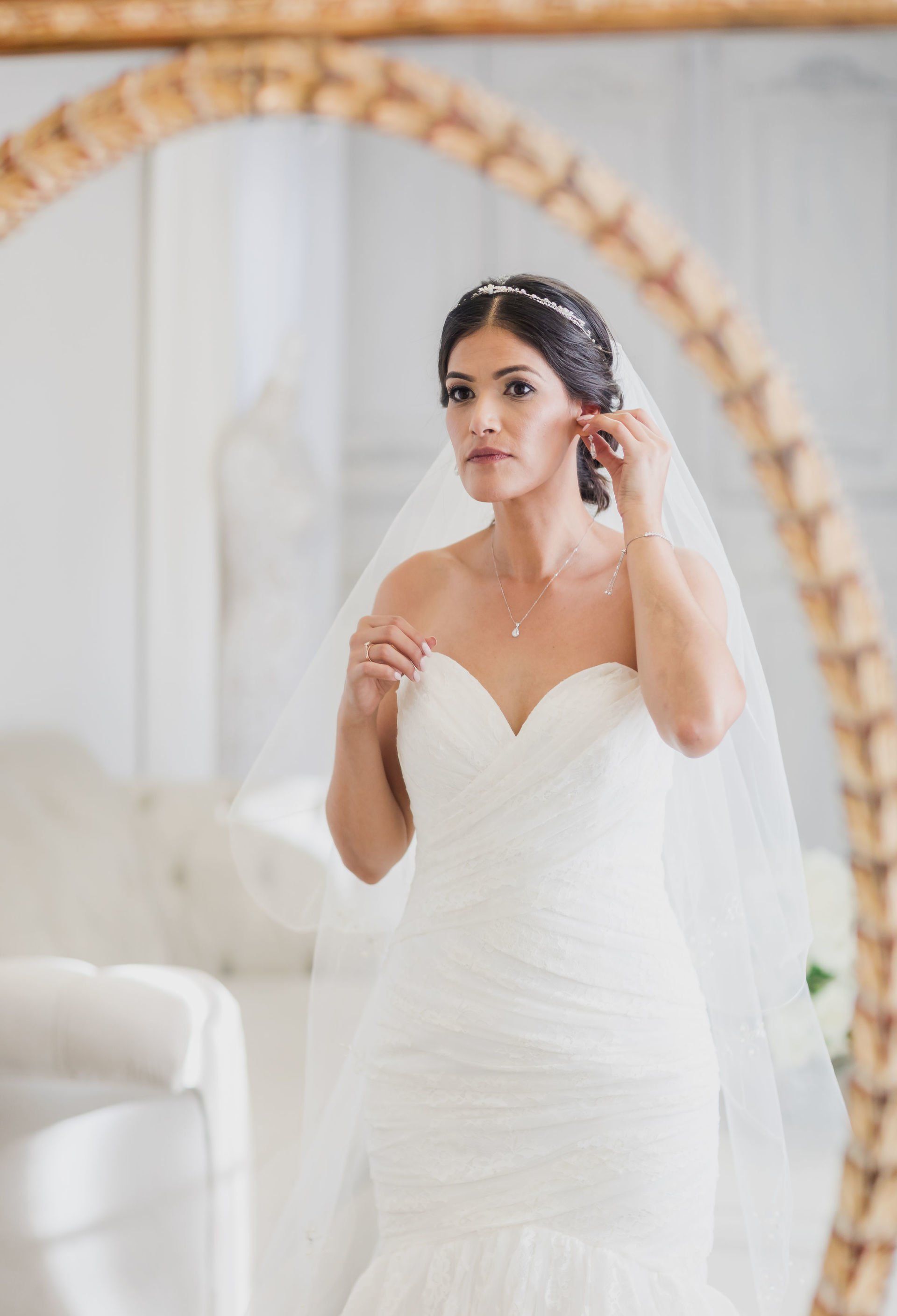 A bride is putting on her veil in front of a mirror.