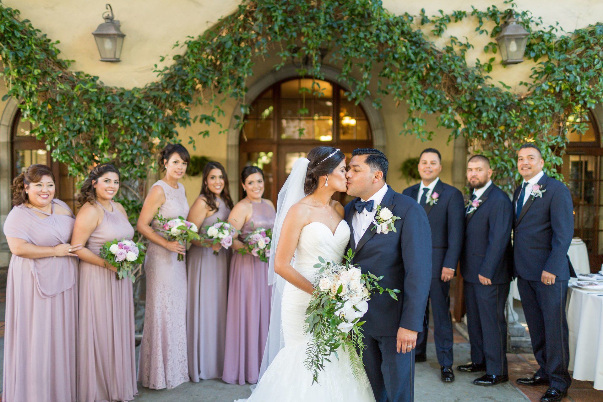 A bride and groom kissing in front of their wedding party.