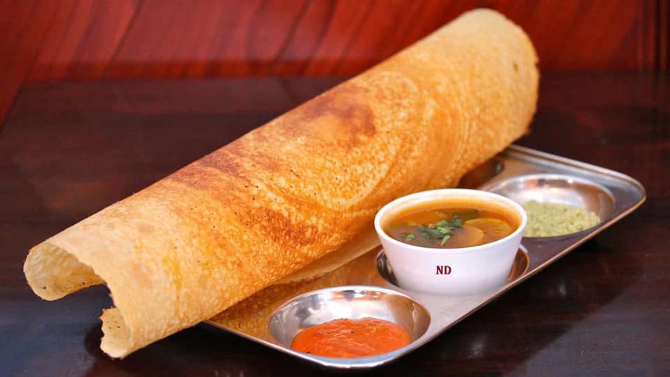 A dosa is sitting on a tray next to a bowl of soup.