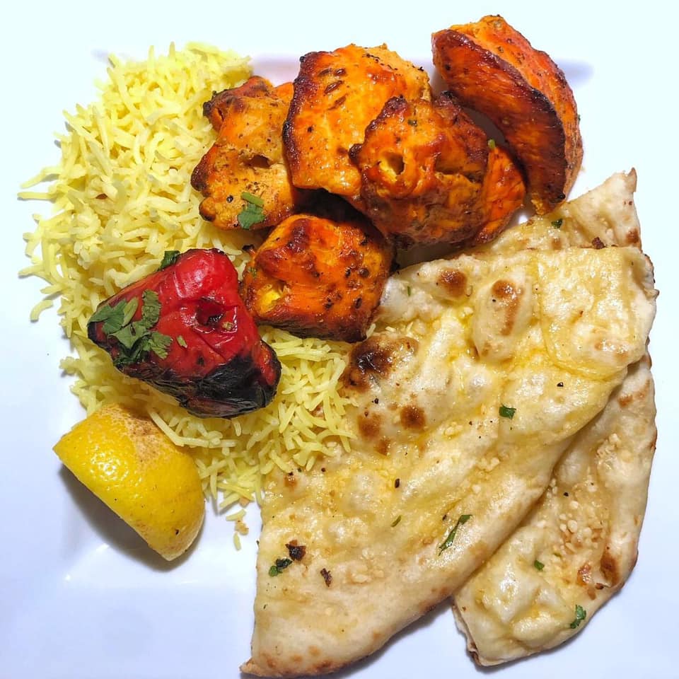 A white plate topped with rice chicken and naan bread