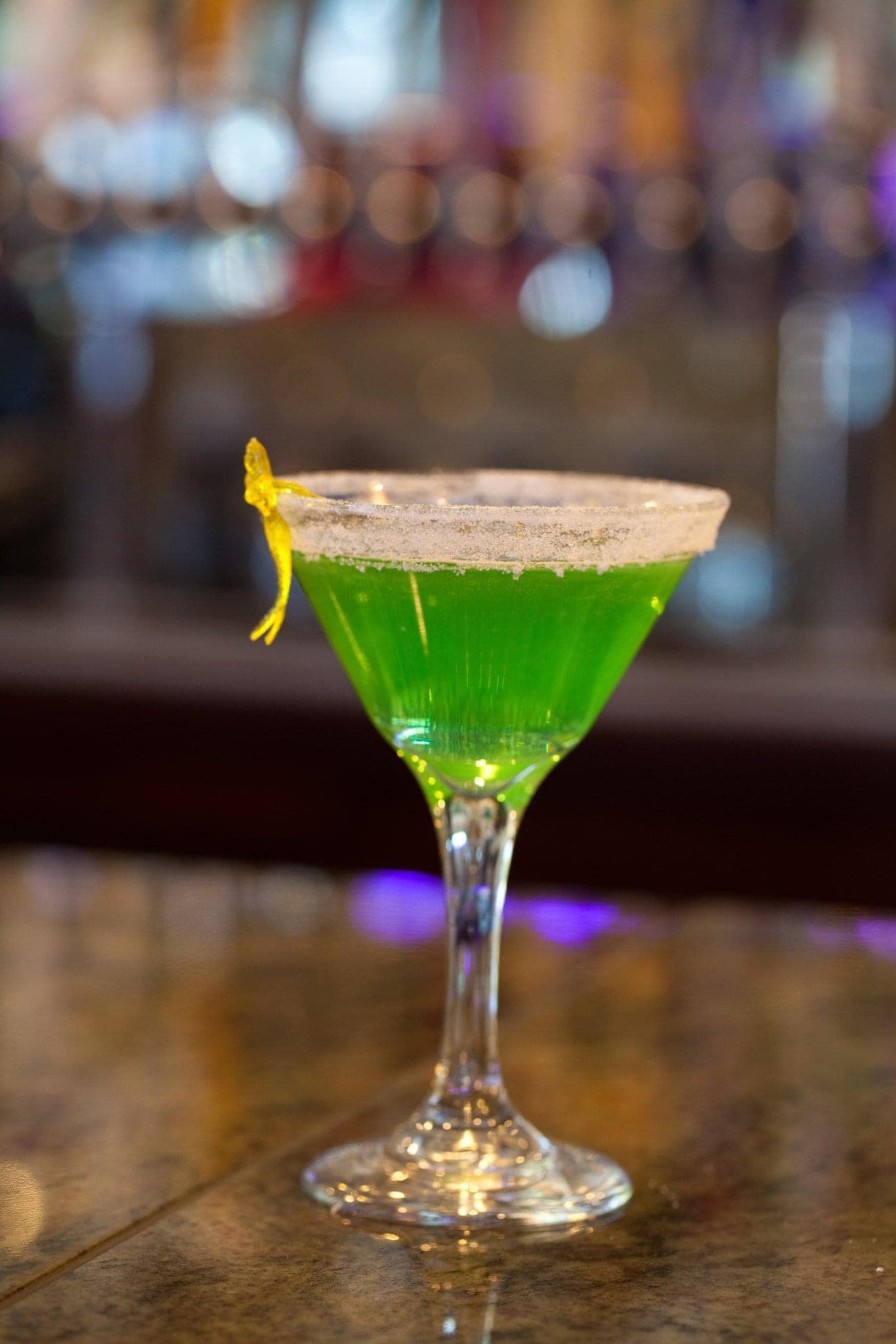 A green cocktail in a martini glass on a table.