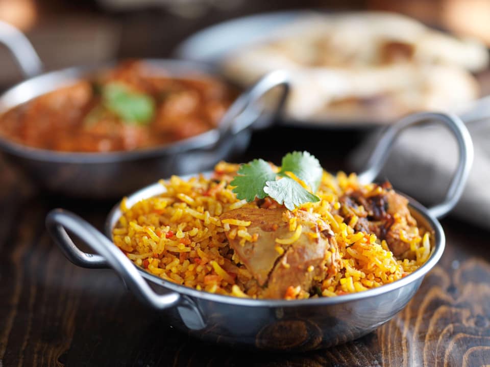 A bowl of chicken biryani is on a wooden table.