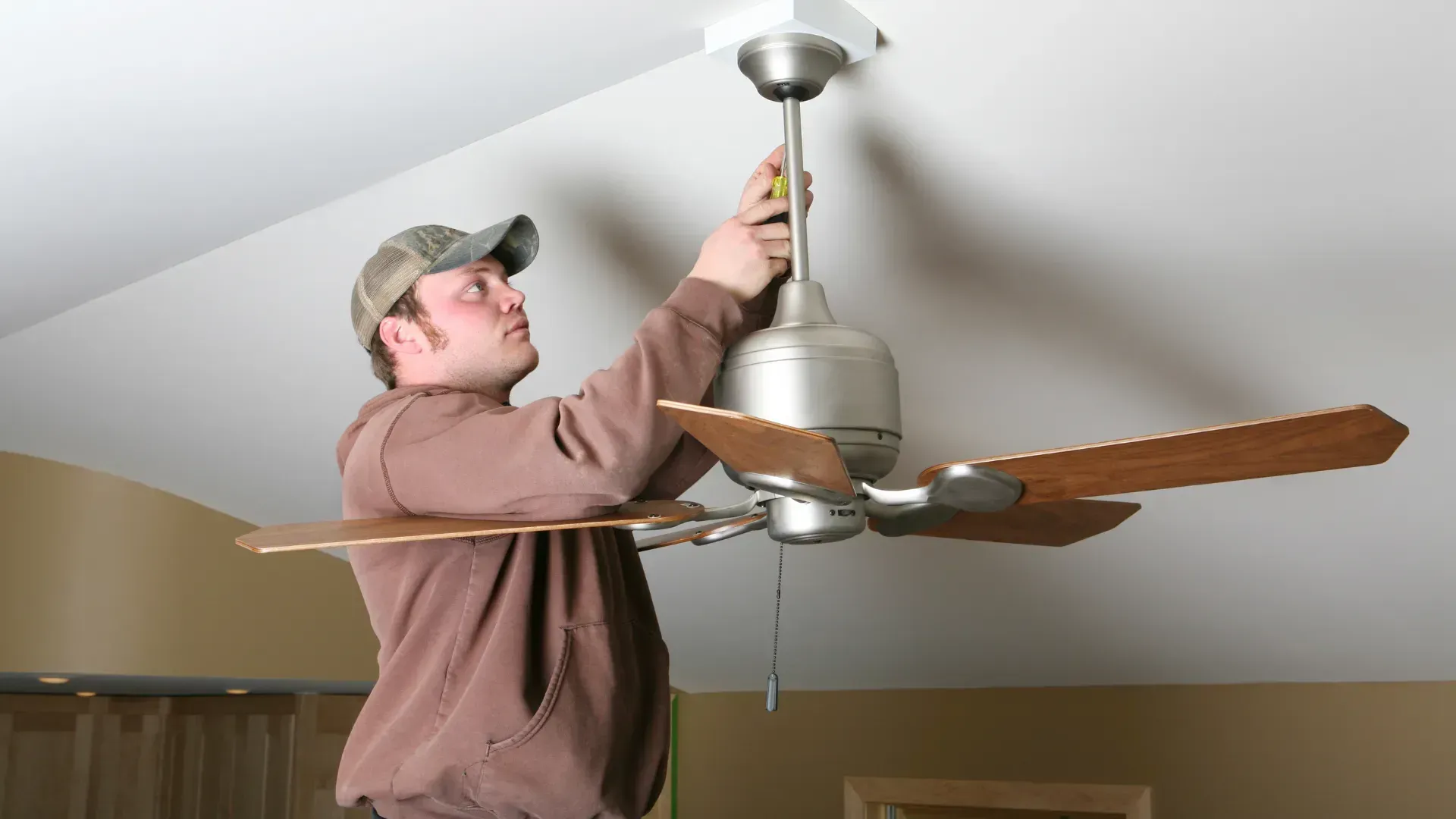 A man is installing a ceiling fan in a living room