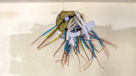 A bunch of wires are coming out of a hole in a wall.