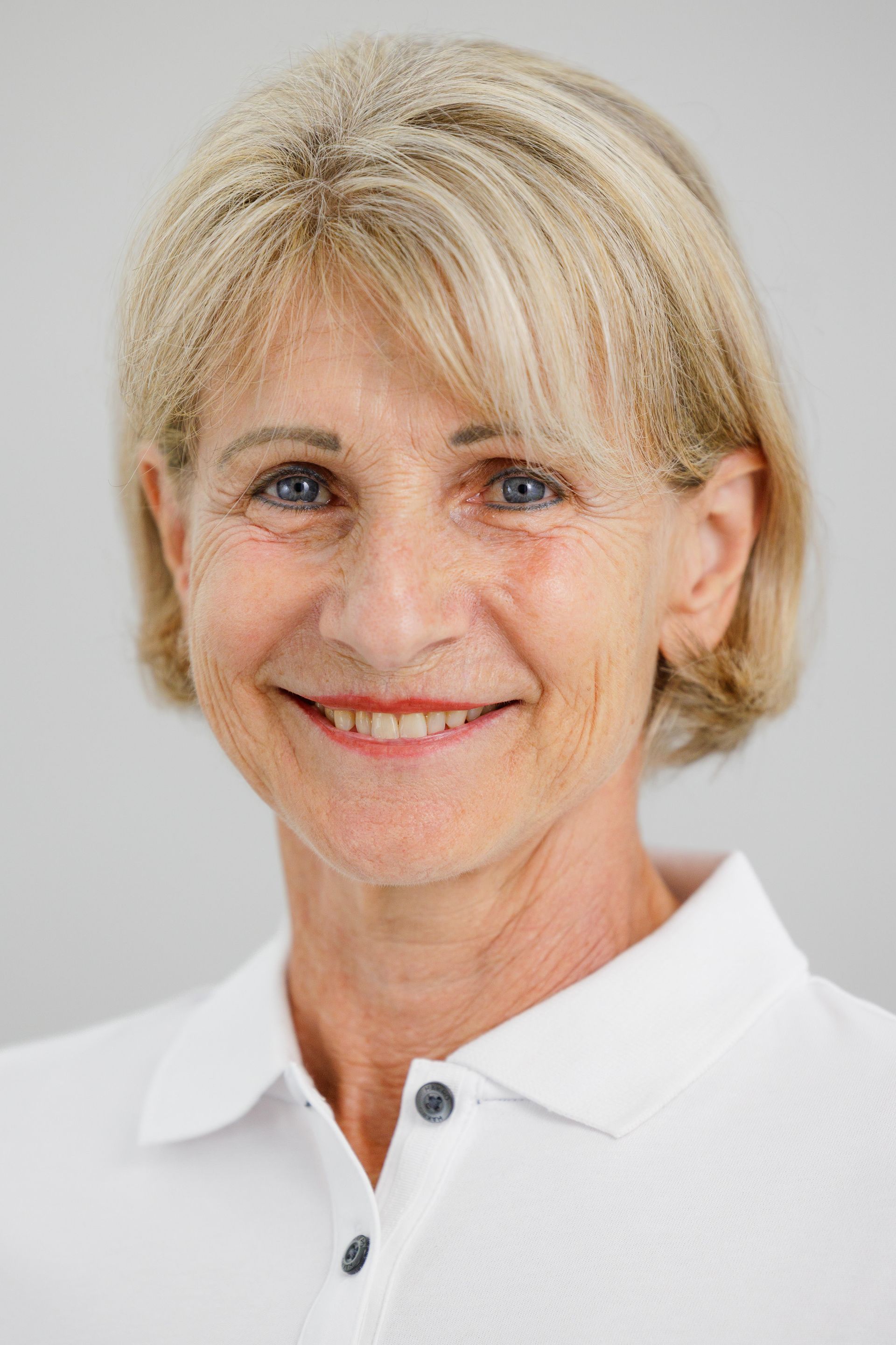 Lächelnde ältere Frau mit blonden Haaren und weissem Poloshirt.