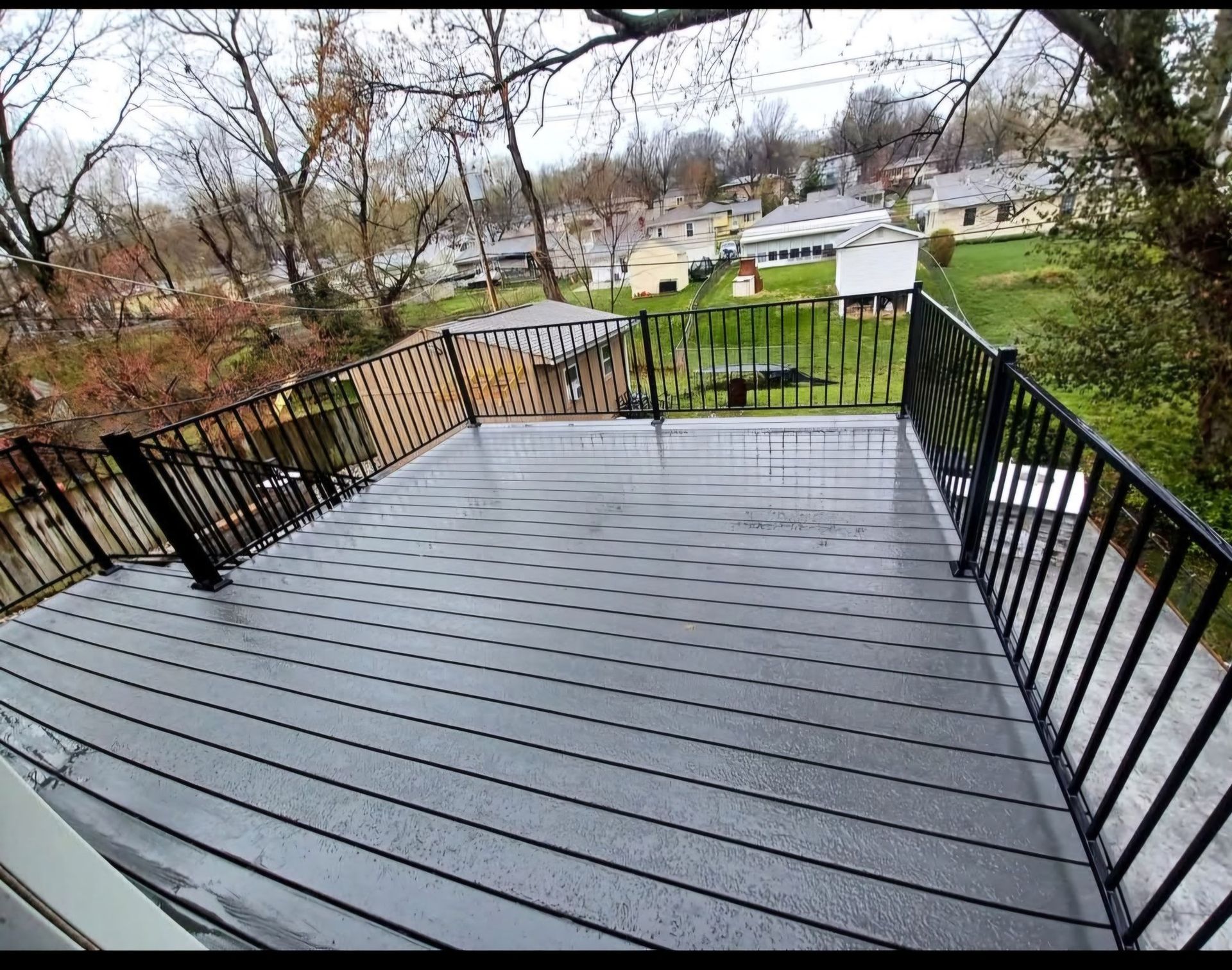 A gray deck with a black railing and a view of a residential area.