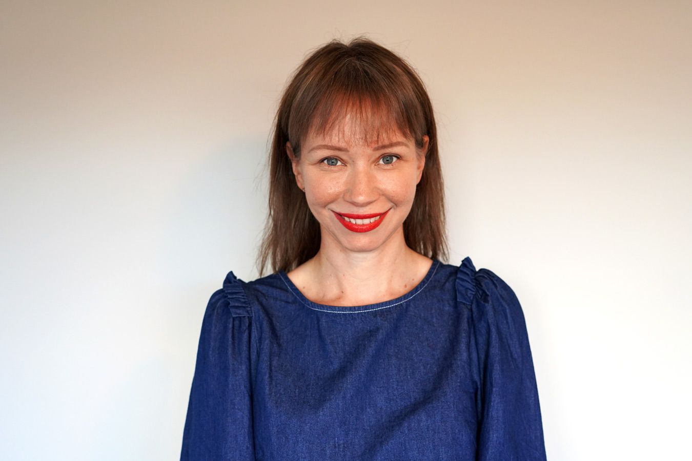 A Woman Wearing A Blue Dress And Red Lipstick Is Smiling For The Camera — Resonance Health Studio in Wauchope, NSW