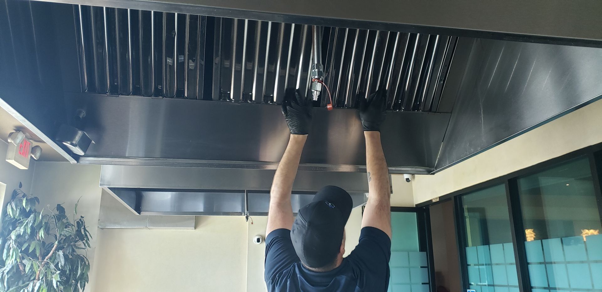 Person in a kitchen, wearing gloves, cleaning the exhaust hood filters.
