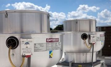 Three large rooftop ventilation units with silver exteriors, under a blue sky.
