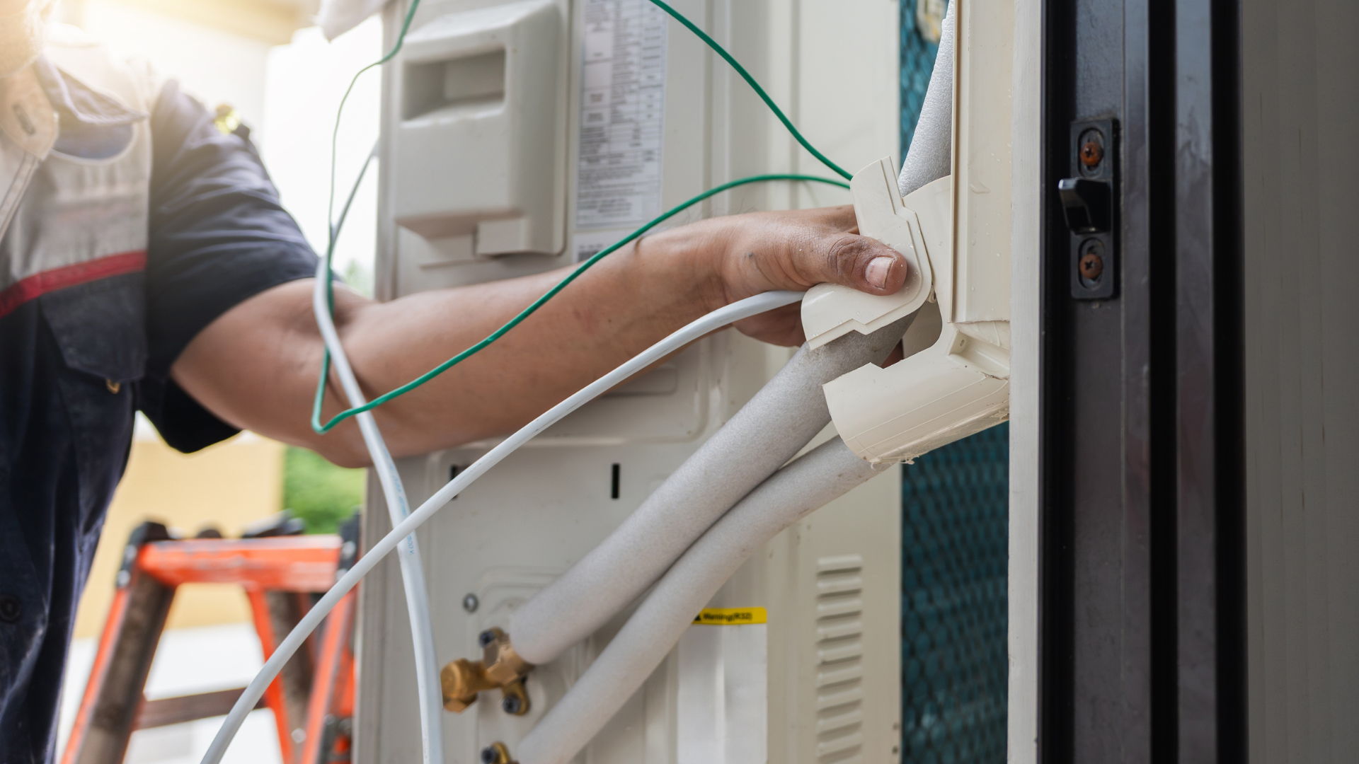 A technician in a uniform works on the wiring and insulation of an outdoor air conditioning unit.