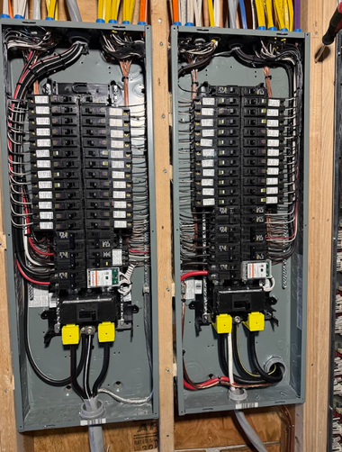 Two side-by-side electrical breaker panels installed on wooden studs, filled with rows of labeled circuit breakers.
