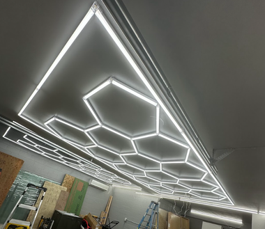 A ceiling installation of interconnected white LED hexagonal light tubes in a room under construction.