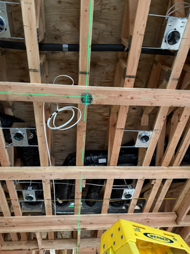 A construction view of wooden ceiling joists with recessed lighting housings, electrical wiring, and ductwork installed.