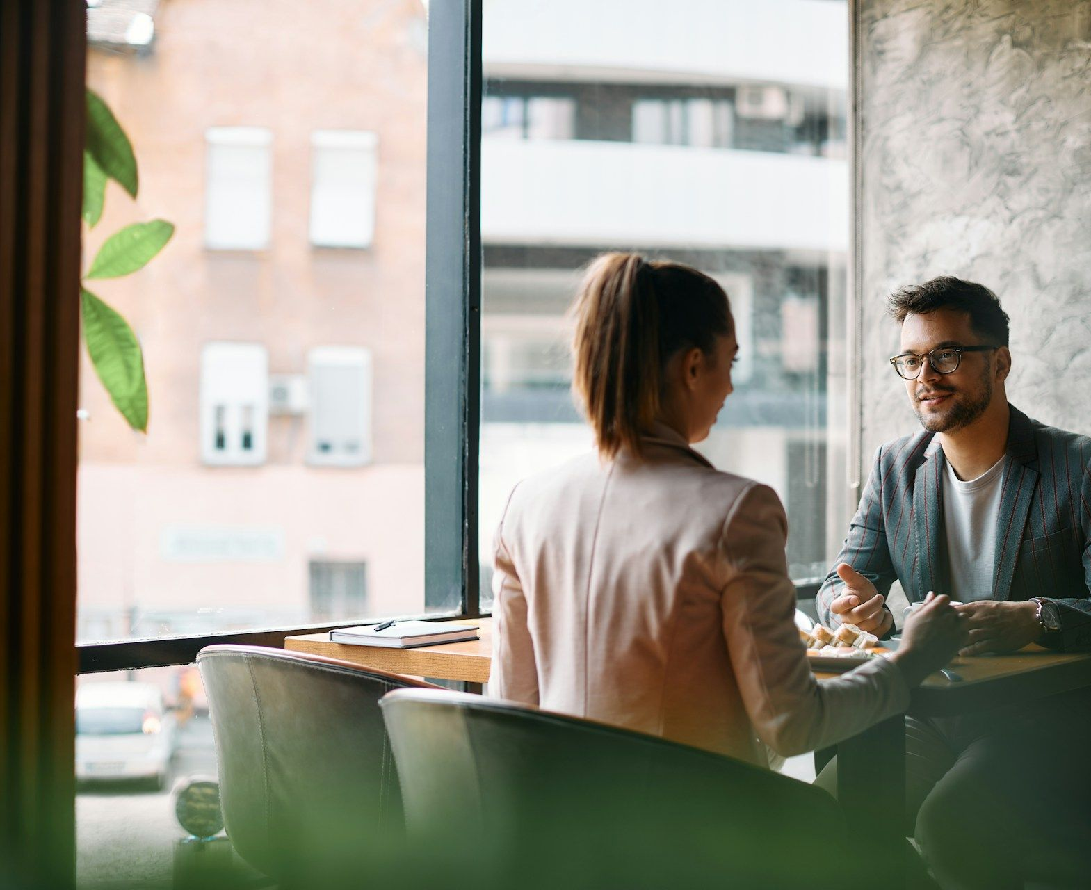 Woman in glasses on the phone, smiling, looking at papers, wearing a patterned blazer.