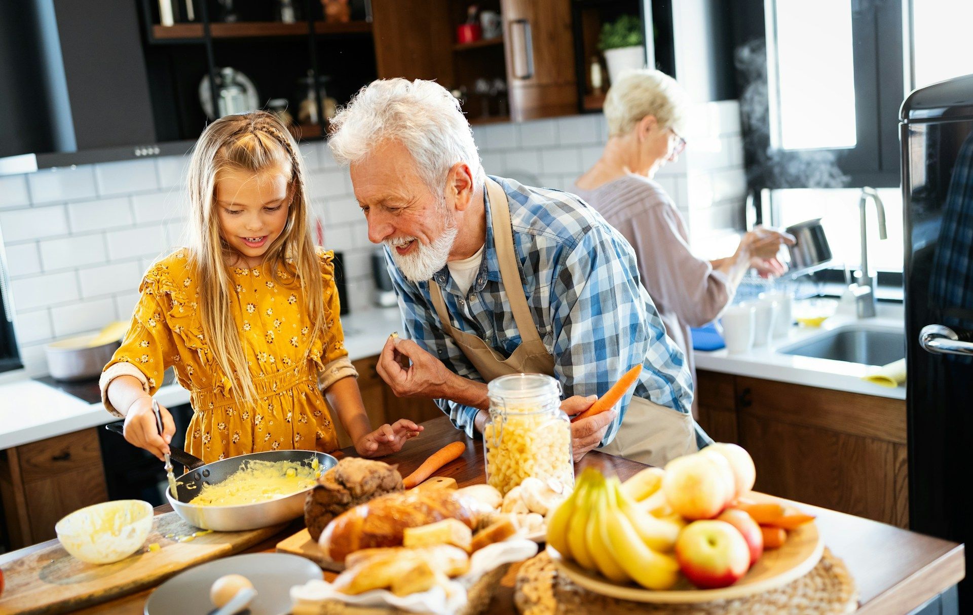 Woman in glasses and blazer types on laptop at a wooden table, notebook and phone nearby, with flowers in the background.