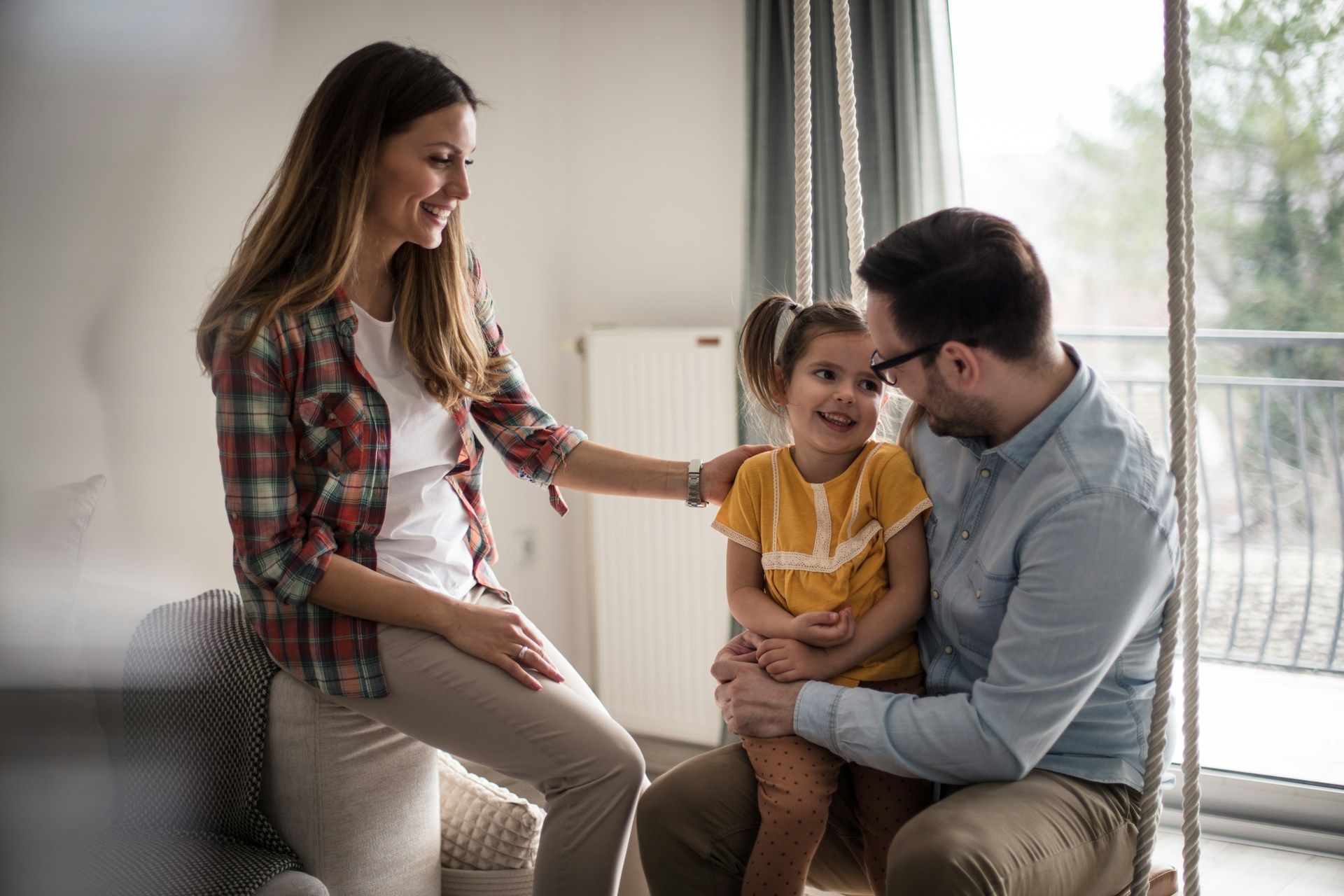 Woman in glasses and blazer types on laptop at a wooden table, notebook and phone nearby, with flowers in the background.